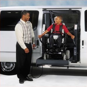 Boy on wheelchair lift in van with man standing next to him